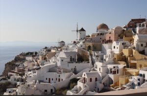 A panoramic view of Oia town from a hilltop, showcasing white buildings and blue domes against a clear sky.
