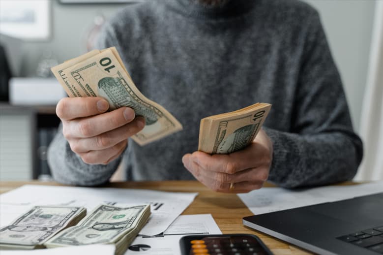 A man holds cash in front of a laptop, suggesting a financial transaction or online shopping scenario.10 financial still