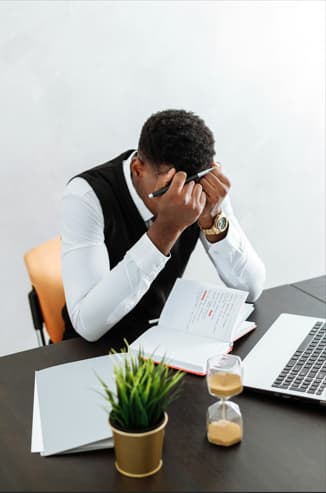 A man sits at a desk, resting his head in his hands, conveying a sense of stress or frustration.10 financial still